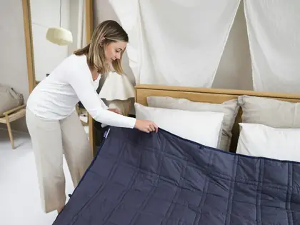 Person spreading a blue blanket over a bed